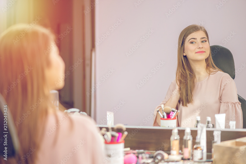 Woman in a beauty salon looks at her reflection in the mirror with lamps and checks hairstyle and makeup Woman in a beauty salon looks at her reflection in the mirror with lamps and checks hairstyle and makeup