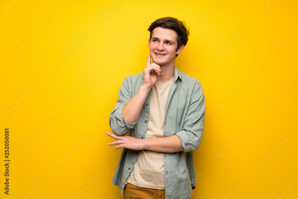 Teenager man over yellow wall thinking an idea while looking up Teenager man over yellow wall thinking an idea while looking up