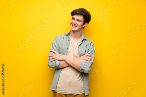 Teenager man over yellow wall keeping the arms crossed while smiling