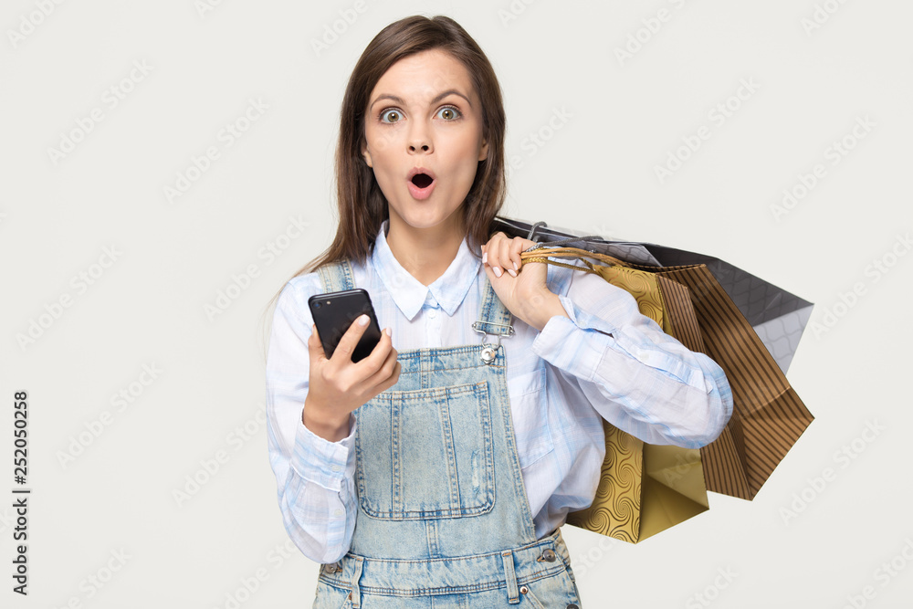 Φωτογραφία Amazed girl holding bags phone surprised by app shopping sale