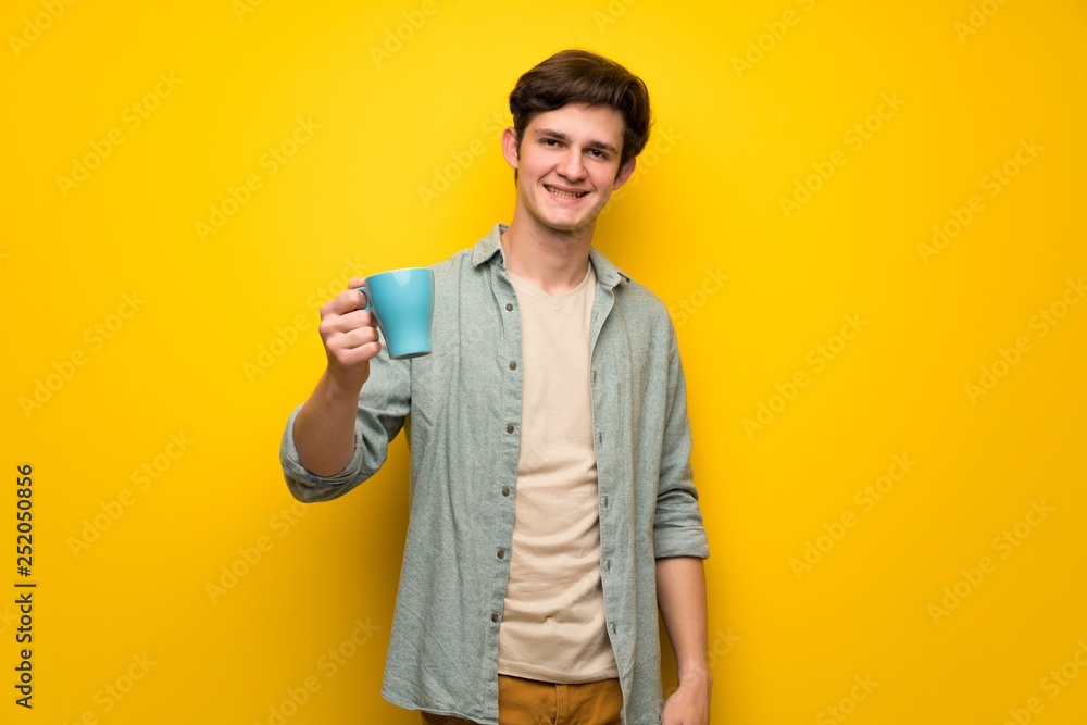 Teenager man over yellow wall holding a hot cup of coffee Teenager man over yellow wall holding a hot cup of coffee
