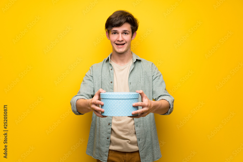 Teenager man over yellow wall surprised because has been given a gift Teenager man over yellow wall surprised because has been given a gift