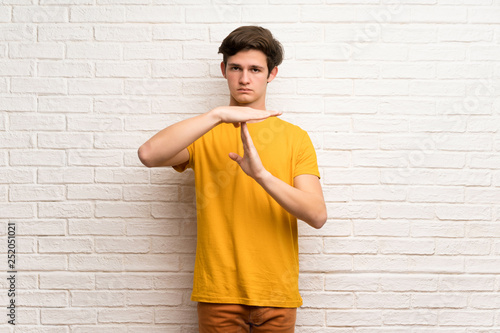 Teenager man over white brick wall making time out gesture