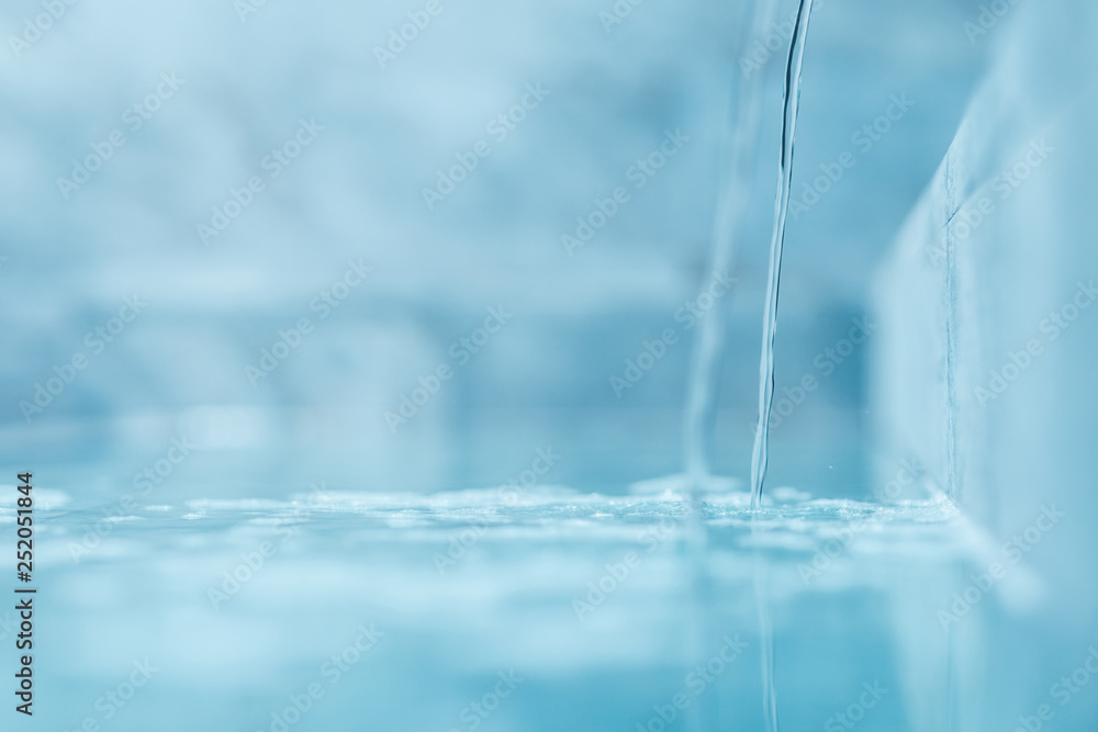 a trickle of crystal clear water is poured into the pool. Selective focus very blurred macro shot with shallow DOF