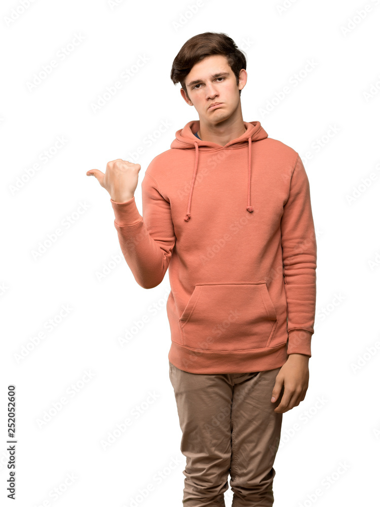 Teenager man with sweatshirt unhappy and pointing to the side over isolated white background Teenager man with sweatshirt unhappy and pointing to the side over isolated white background