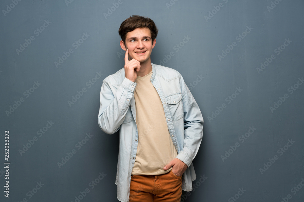 Teenager man with jean jacket over grey wall thinking an idea while looking up