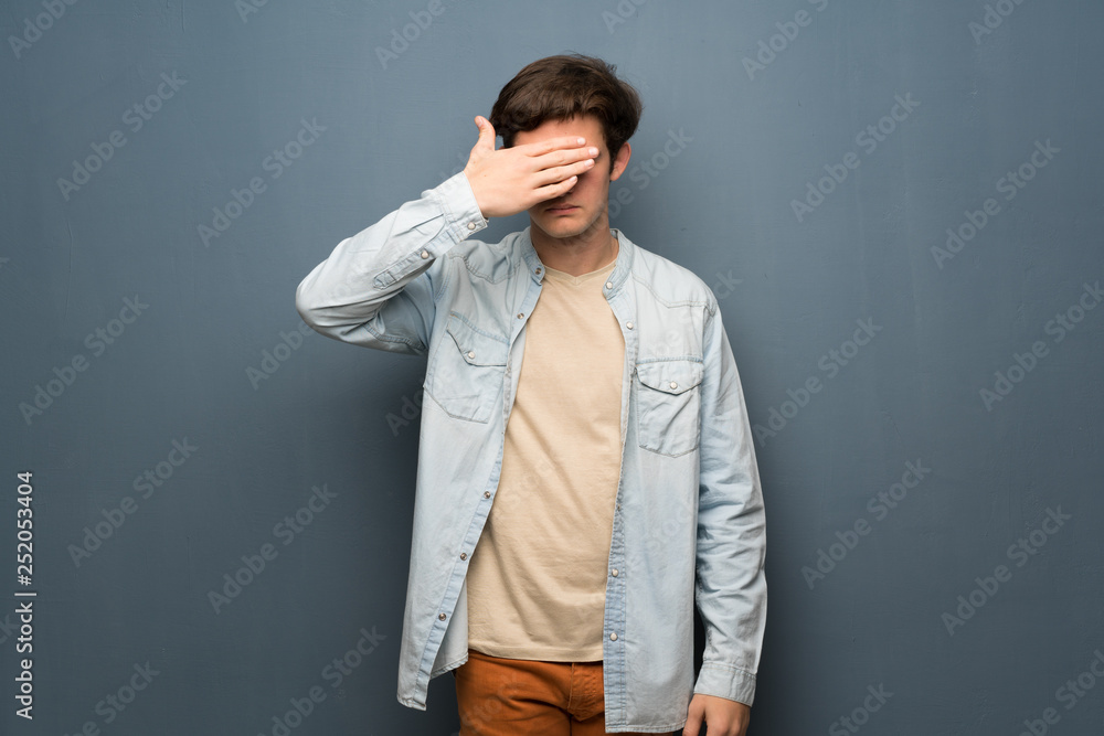 Teenager man with jean jacket over grey wall covering eyes by hands. Do not want to see something