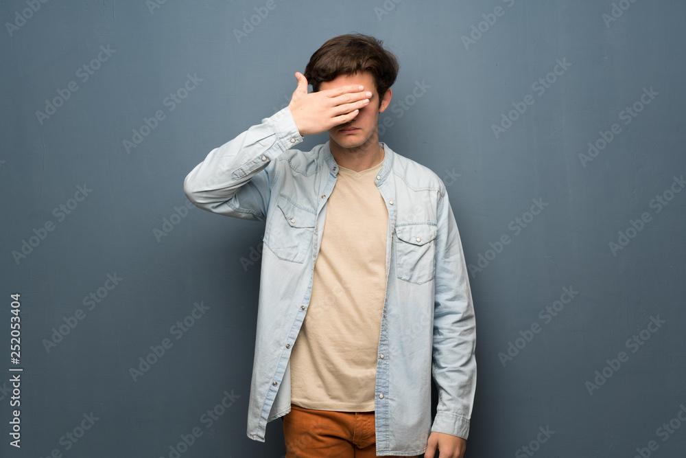 Fototapeta premium Teenager man with jean jacket over grey wall covering eyes by hands. Do not want to see something