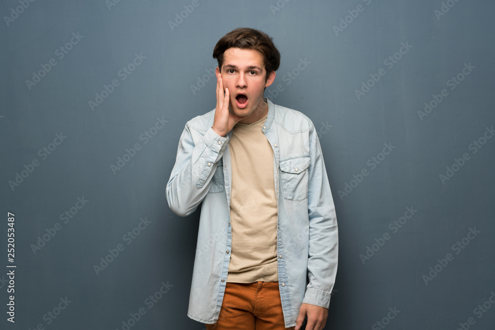 Teenager man with jean jacket over grey wall with surprise and shocked facial expression