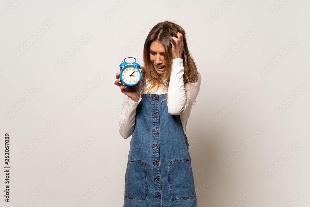 Beautiful woman over isolated white wall restless because it has become late and holding vintage alarm clock Beautiful woman over isolated white wall restless because it has become late and holding vintage alarm clock