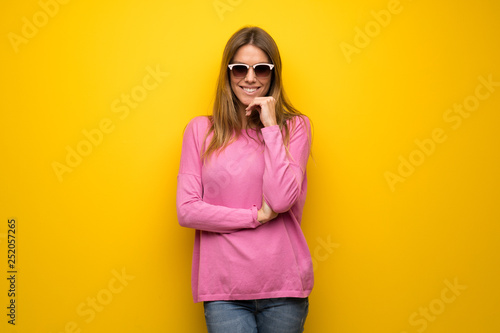 Woman with pink sweater over yellow wall with glasses and smiling © luismolinero