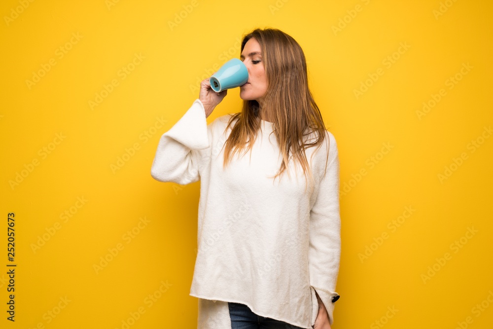 Blonde woman over yellow wall holding a hot cup of coffee Blonde woman over yellow wall holding a hot cup of coffee