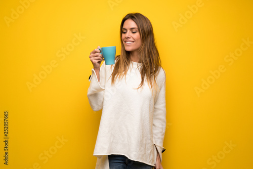 Blonde woman over yellow wall holding a hot cup of coffee