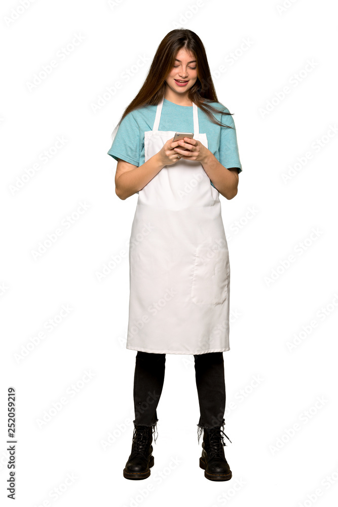 Full-length shot of Girl with apron sending a message with the mobile on isolated white background Full-length shot of Girl with apron sending a message with the mobile on isolated white background
