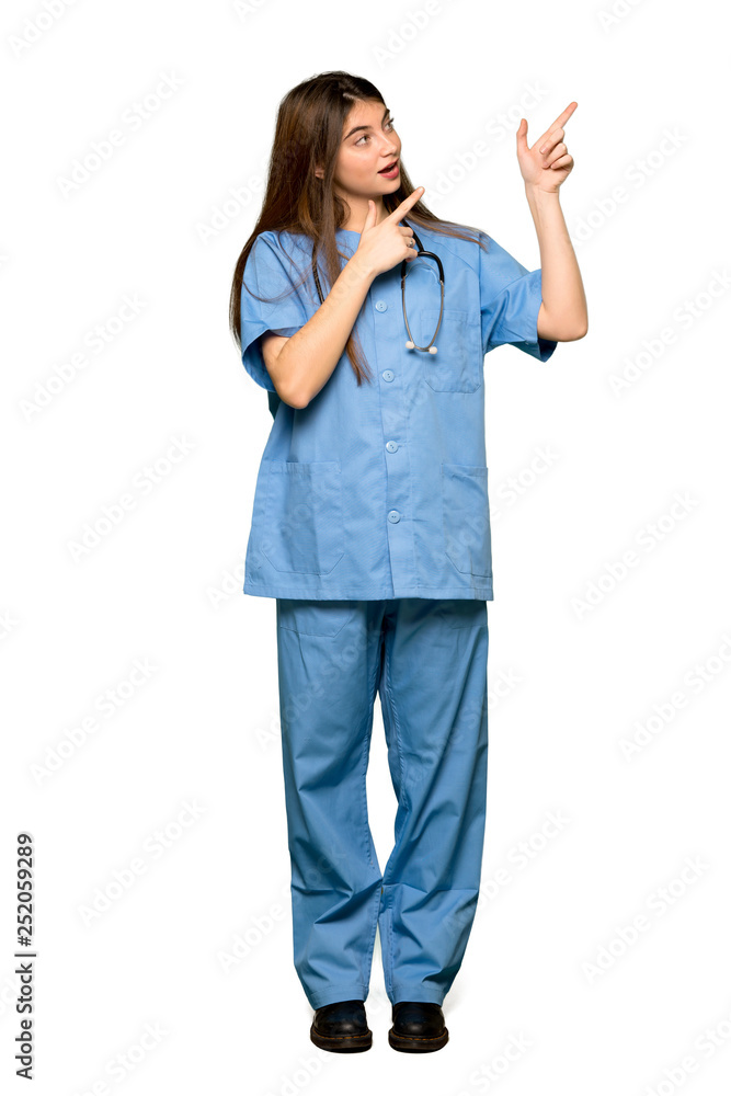 Full-length shot of Young nurse pointing with the index finger and looking up on isolated white background Full-length shot of Young nurse pointing with the index finger and looking up on isolated white background