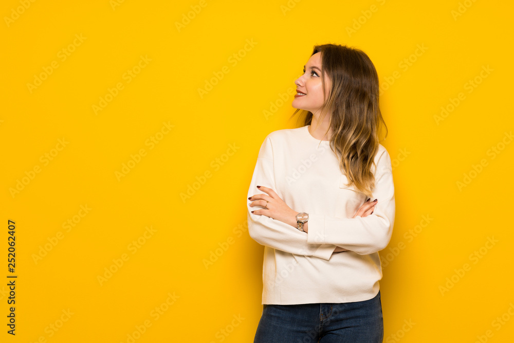 Teenager girl over yellow wall keeping the arms crossed while smiling Teenager girl over yellow wall keeping the arms crossed while smiling