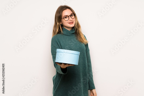 Teenager girl over white wall holding a gift in hands