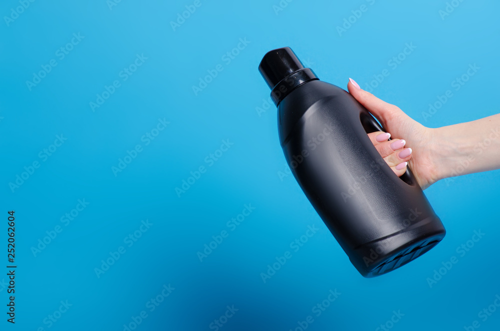 Black bottle laundry gel in hand on blue background isolation Black bottle laundry gel in hand on blue background isolation