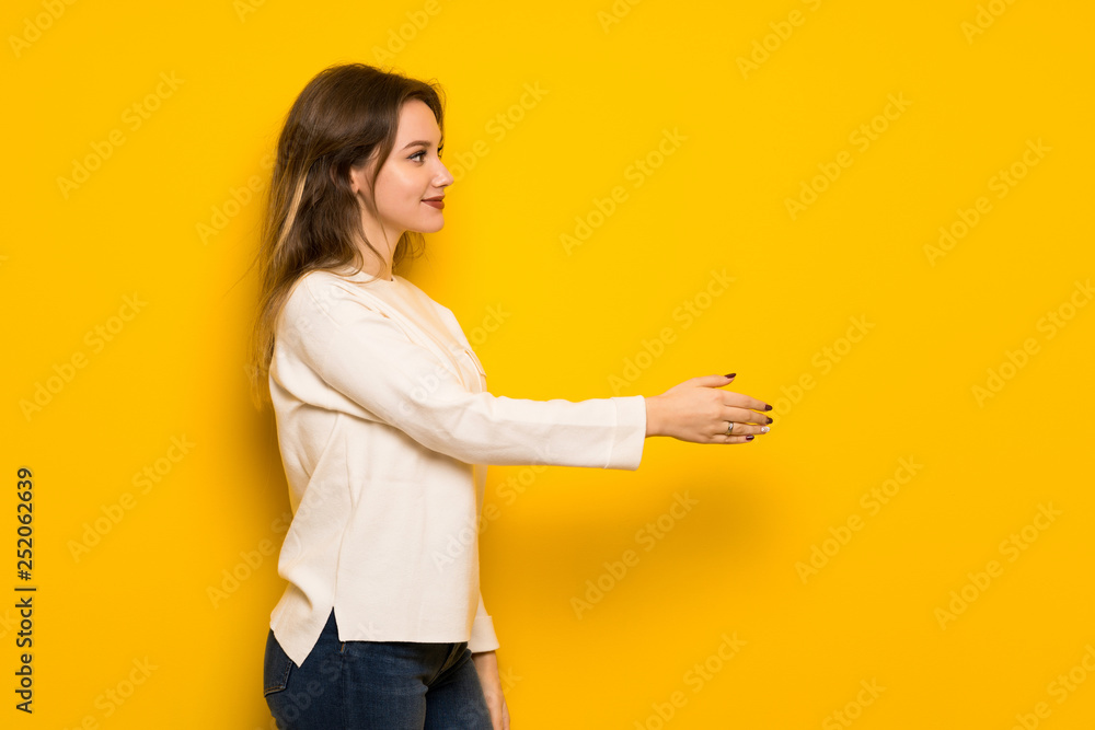 Teenager girl over yellow wall handshaking after good deal Teenager girl over yellow wall handshaking after good deal