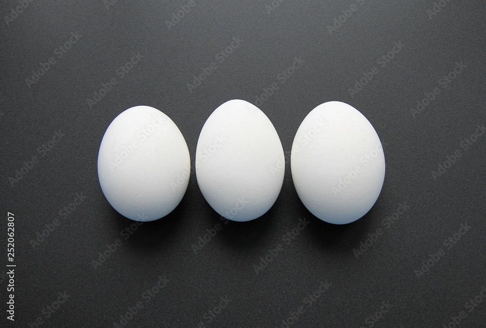 Three white eggs in the shell are on a black background Three white eggs in the shell are on a black background