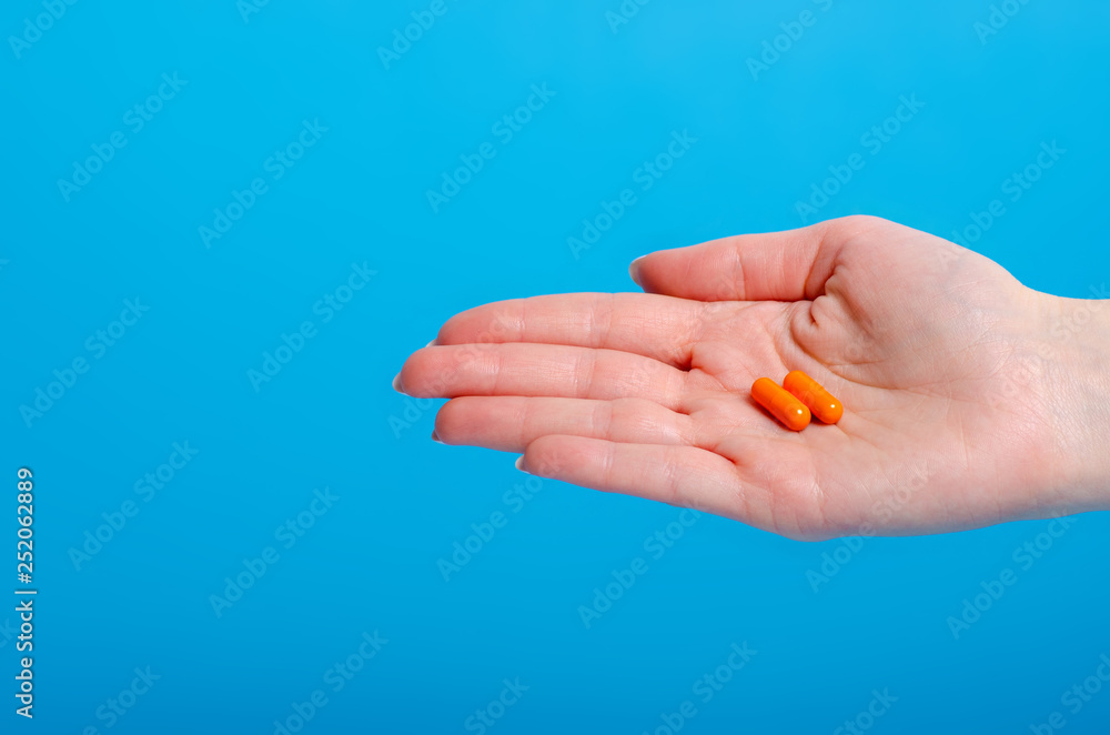 Orange pills capsule in hand pharmasy medecine on blue background