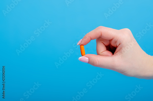 Orange pills capsule in hand pharmasy medecine on blue background