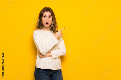 Teenager girl over yellow wall surprised and pointing side