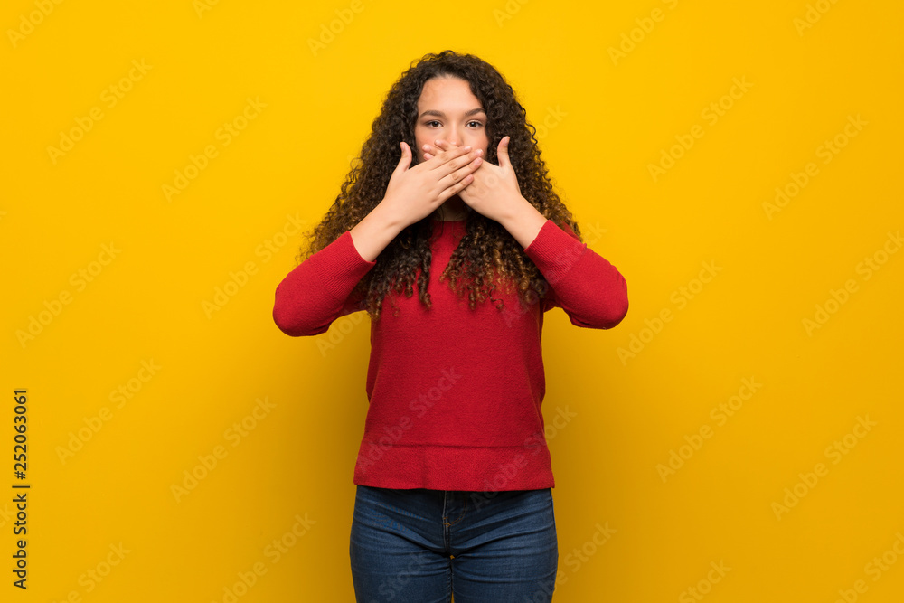 Teenager girl with red sweater over yellow wall covering mouth with hands for saying something inappropriate