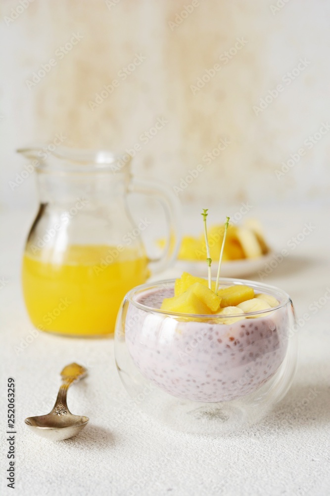 Chia pudding with mango pulp in beautiful glasses with green mint leaves and cut fresh ripe tropical fruit, orange juice for breakfast on a light background - raw vegetarian sweet organic dessert. Chia pudding with mango pulp in beautiful glasses with green mint leaves and cut fresh ripe tropical fruit, orange juice for breakfast on a light background - raw vegetarian sweet organic dessert.