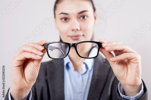 Businesswoman holding eyeglasses in hands on gray background