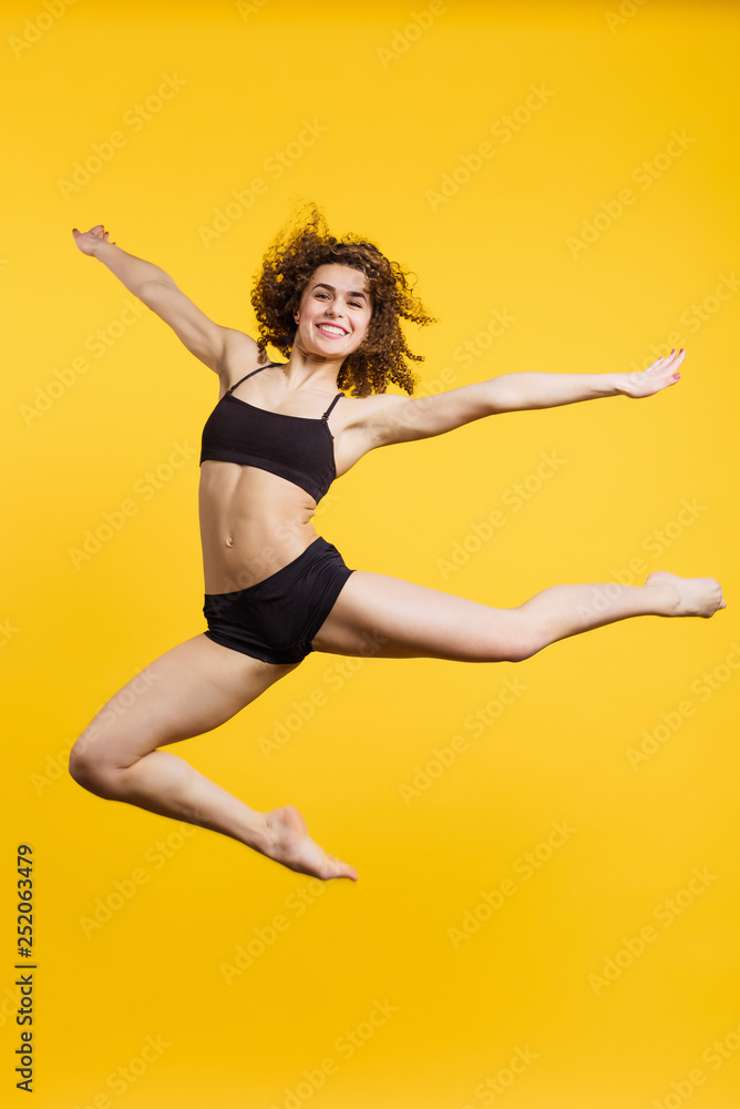 beautiful gymnast in a jump on a yellow background