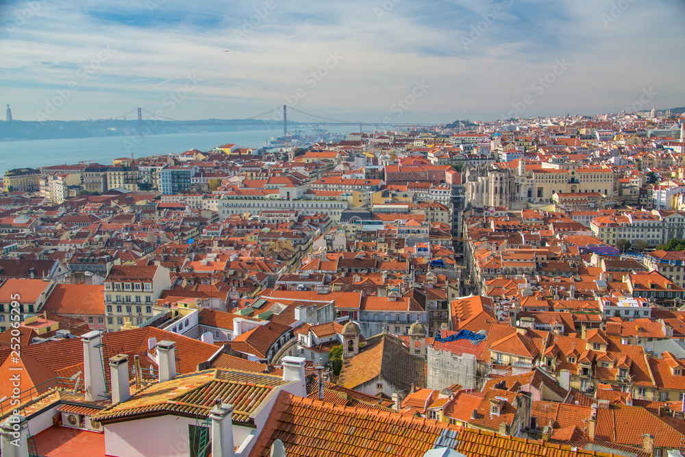 View of the streets and the orange roofs of the old town. Lisbon, Portugal. In the distance, see the bridge of April 25 and the statue of Christ. View from the walls of the castle of St. George