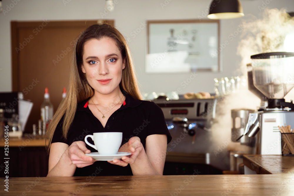 Beautiful female barista is working in coffee shop. Attractive woman is standing behind the bar counter, making coffee and welcomes customers. Beautiful female barista is working in coffee shop. Attractive woman is standing behind the bar counter, making coffee and welcomes customers.
