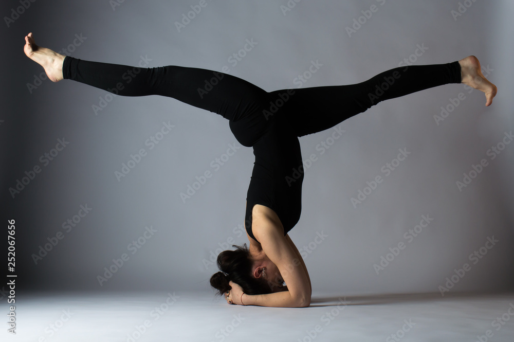 Beautiful young dark-haired girl in a black uniform and does yoga. Studio photos.
