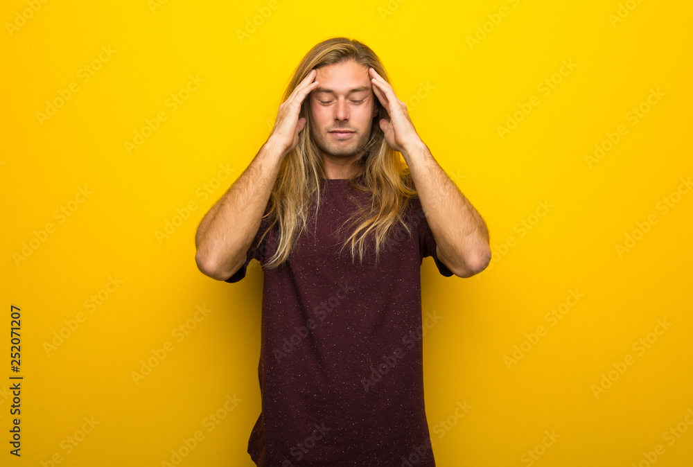 Blond man with long hair over yellow wall unhappy and frustrated with something