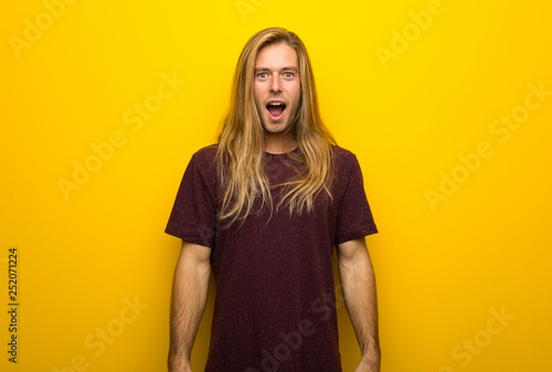 Photography Blond man with long hair over yellow wall with surprise and shocked facial expre