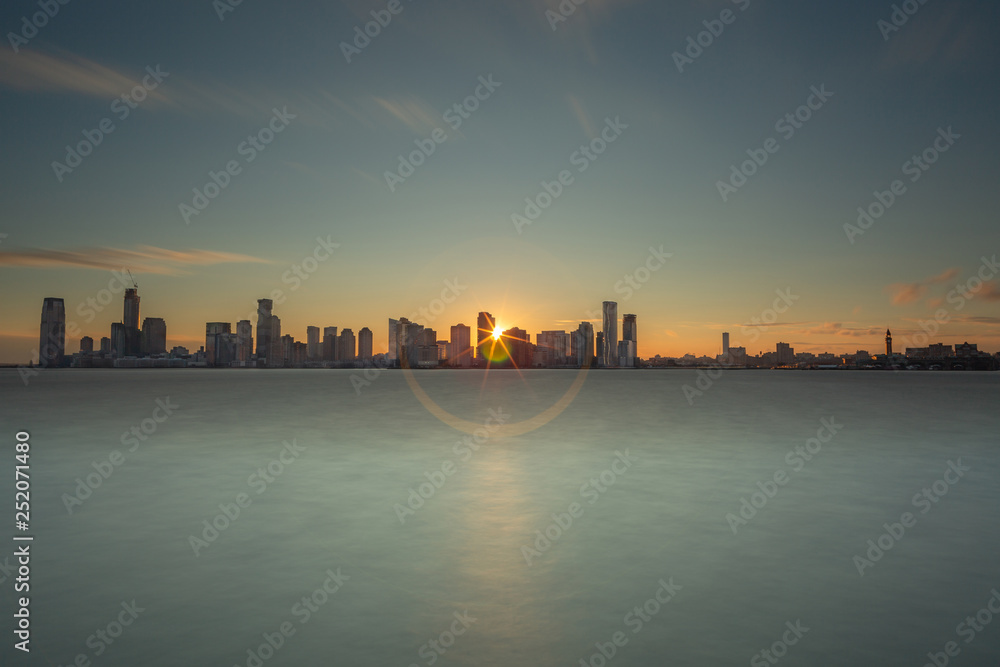 Fototapeta premium View on Jersey city with direct sun from hudson river with long exposure