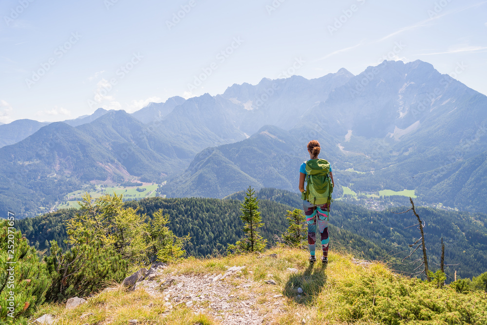 Young woman wearing backpack is admiring the valley view from top of a mountain. Travel and adventure concept. Healthy lifestyle and hiking concept.