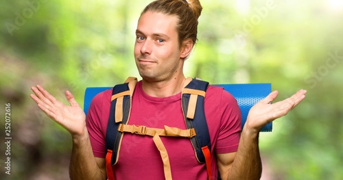 Hiker man with mountain backpacker making unimportant gesture while lifting the shoulders in the mountain