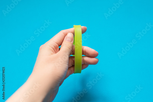 Girl puts on green bracelet on blue background. Greenpeace concept and vote for nature. Music festival branding empty wristband. 