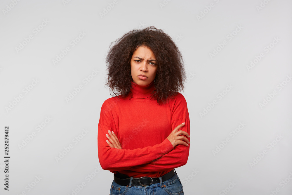 Serious suspicious latino woman with curly afro hair standing with crossed hands and frowning, expressing distrustfulness and disappointment, over white background - obrazy, fototapety, plakaty 
