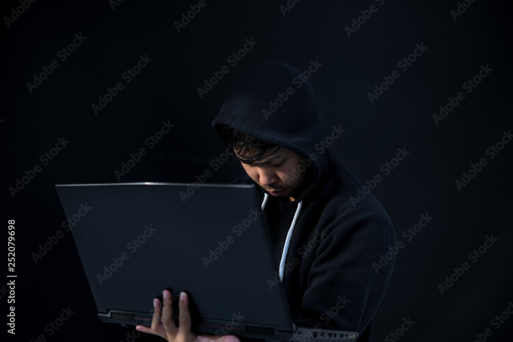 Asian hacker in black hood on black background,Hack password,hacking safety systems to steal information Asian hacker in black hood on black background,Hack password,hacking safety systems to steal information