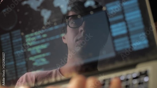 Double exposure: man programmer in glasses working at a laptop. Programmer writes blue code, reflection in the monitor