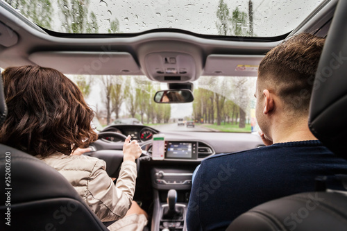 Beautiful couple sitting on the front passenger in vehicle. woman is driving a car. view from a back of young pair. travel and adventure concept