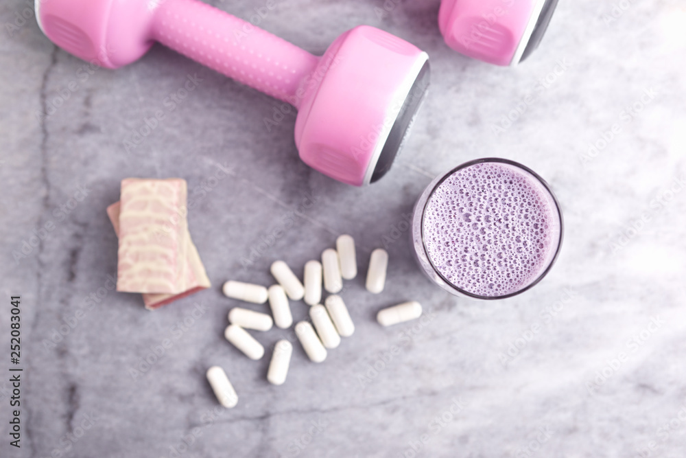 Glass of Protein Shake with milk and blueberries. BCAA capsules, Protein bar in two pieces and pink dumbbells in background. Concept for Sport nutrition. Stone background. Top view. Copy space. Glass of Protein Shake with milk and blueberries. BCAA capsules, Protein bar in two pieces and pink dumbbells in background. Concept for Sport nutrition. Stone background. Top view. Copy space.