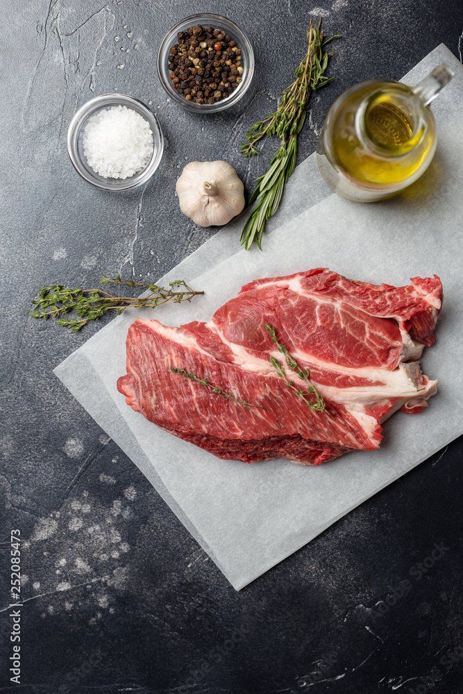 fresh piece of beef tenderloin on craft paper with spices and herbs on black background