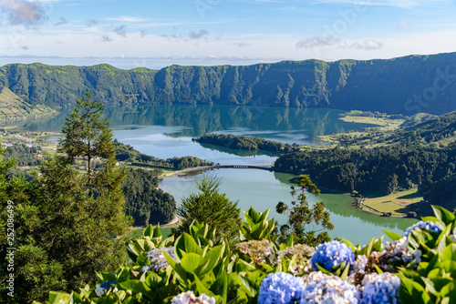 Green and blue lakes seen from above, with a blue sky and lush vegetation around. They are the famous Lagoa Verde and Lagoa Azul, also known as Lagoa das Sete Cidades, on Sao Miguel in the Azores