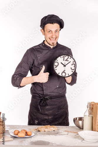 Baker's in black apron holding big clock and pointing finger at them. people, time management and gesture concept photo