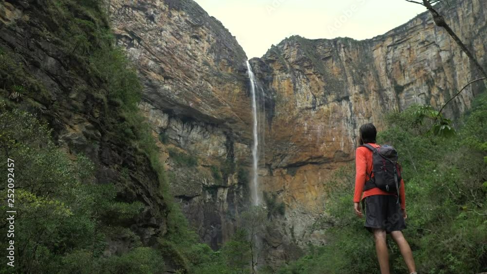 Man climbing hill walking stick in hand and backpack, Waterfall of Tabuleiro in the background Man climbing hill walking stick in hand and backpack, Waterfall of Tabuleiro in the background