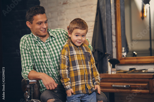 Young handsome father and his little stylish son at barbershop waiting for barber